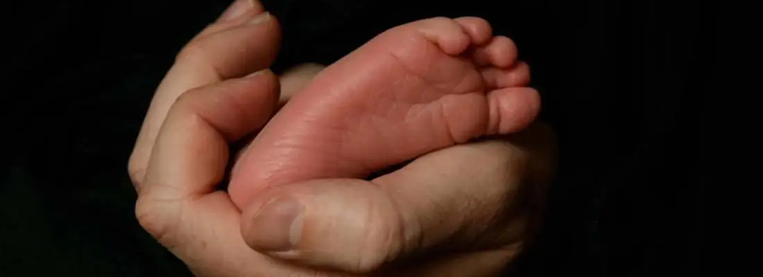 A baby 's foot in the palm of an adult hand.