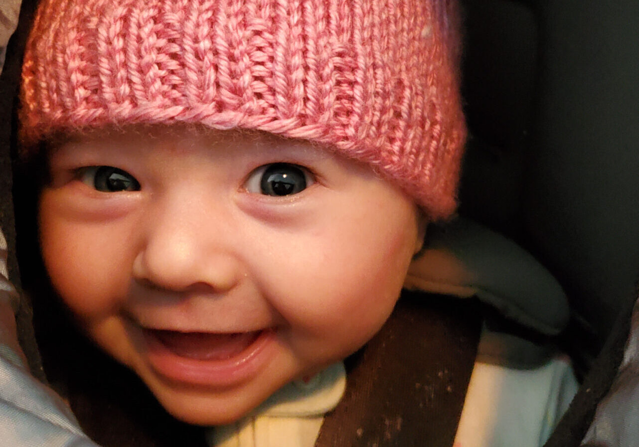 A baby wearing a pink hat and smiling.